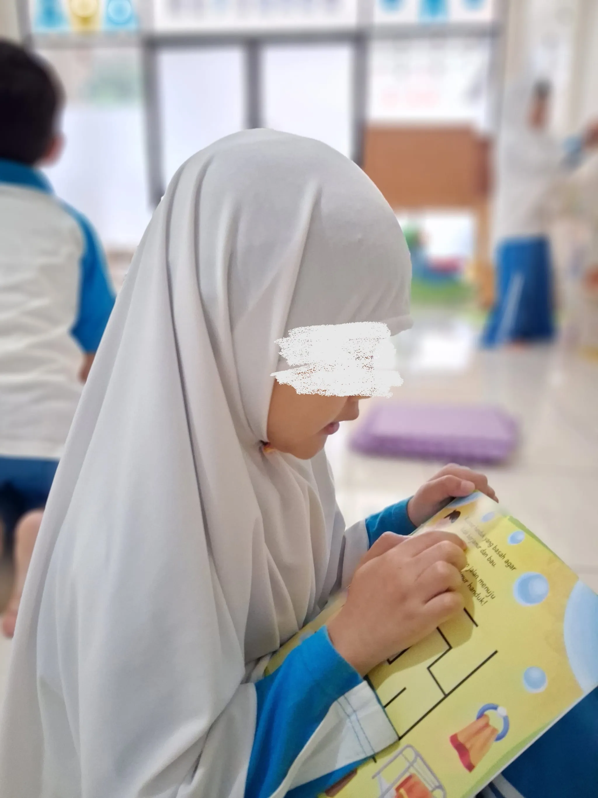 Seorang anak berkerudung putih mengerjakan buku kegiatan bergambar di kelas